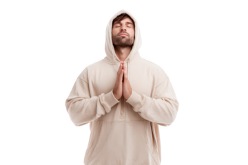 young man in a beige hoodie, standing and praying with his hands together