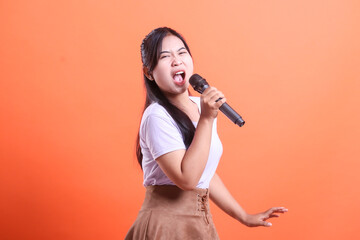 A young asian woman singing passionately into a microphone with a focused expression during a live...