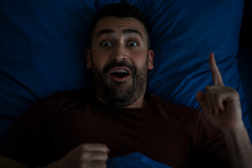 Man having idea while sleeping at night, lying in bed, looking at camera. Creativity, eureka...
