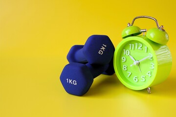 blue barbell and alarm clock on yellow background