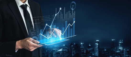 A businessman analyzes digital financial graphs on a tablet against a modern city skyline at night, showcasing concepts of growth, innovation, and technology. Scalp