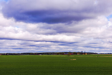 Beautiful view of green agricultural field on background of cloudy sky and distant rural horizon. Sweden.