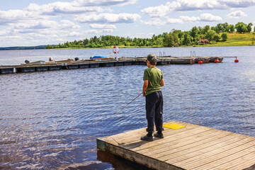 Close up view of boy fishing from wooden pier on background of calm lake water. Sweden.