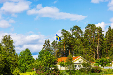 Beautiful view of Swedish country house with national flag on background of green forest and blue sky. Sweden.