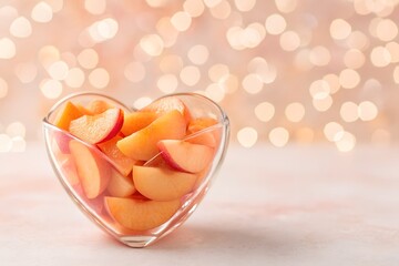 Heart-shaped glass filled with fresh peach slices on a warm bokeh background symbolizing sweetness, love and summer mood. Soft food image perfect for wellness, romance and elegant design concepts.