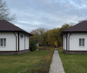 Two houses are placed alongside a path in a park. Trees are changing color in the background