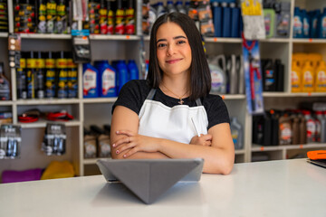 Young woman standing behind a counter in an auto parts retail store with a tablet