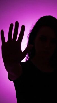 Silhouette of a person holding up their hand in a stop gesture against a pink background. Say no to violence against women, femicide.