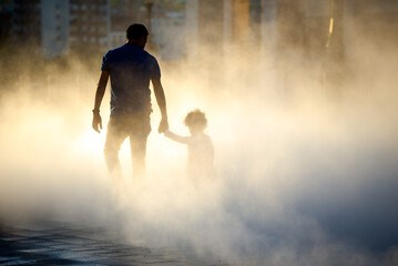 Silhouette of father and son walking hand in hand in fog