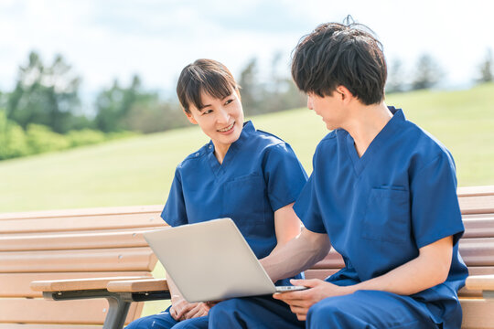Male and female medical staff (occupational therapists and nurses) wearing scrubs looking at a computer on a bench in a hospital or facility