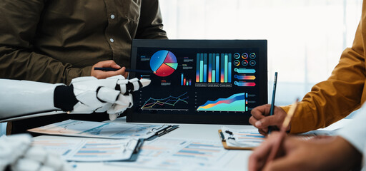 A diverse team collaborates in a modern office, discussing data analysis and insights. The robot interacts with digital displays featuring charts and graphs.Noogenesis