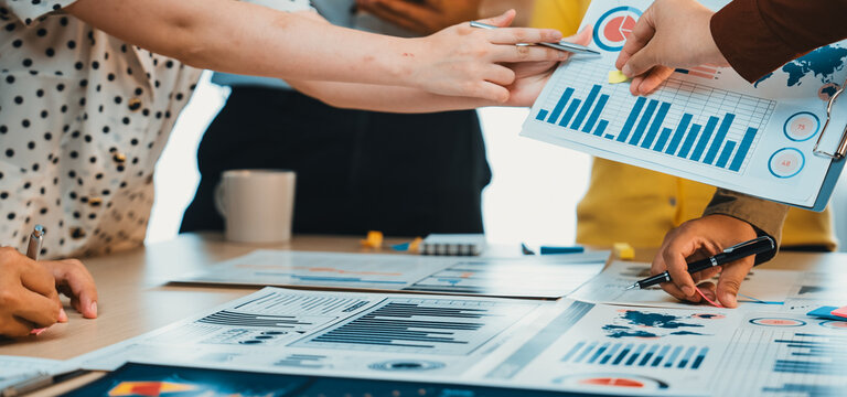 A dynamic scene of a business meeting where diverse professionals analyze data charts and graphs collaboratively on a workspace table, showcasing teamwork and strategy. SACTR - Powered by Adobe