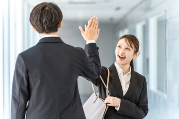 Young businessmen and women exchanging high fives as they pass each other in an office corridor