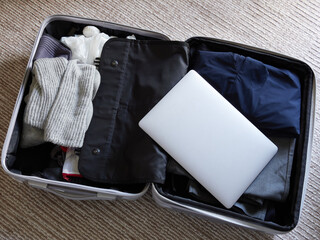 家のリビングの絨毯の上にある出張用のスーツケースと中身の衣服類とノートパソコンの様子