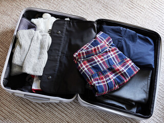 家のリビングの絨毯の上にある出張用のスーツケースと中身の衣服類の様子