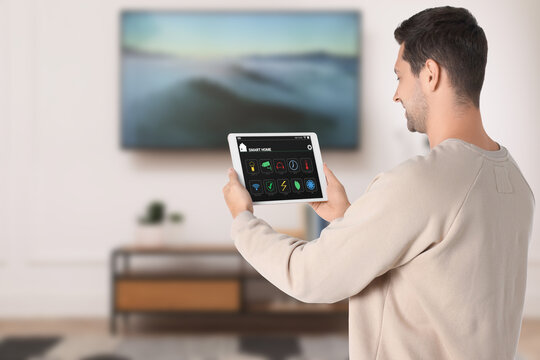 Smart home system. Man using app on tablet computer to control house features in room