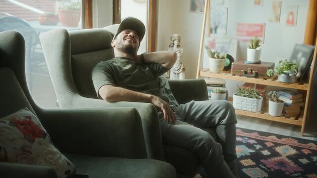 Young man sitting in armchair, holding his neck in discomfort, likely from poor sleep posture or muscle strain in the morning.
