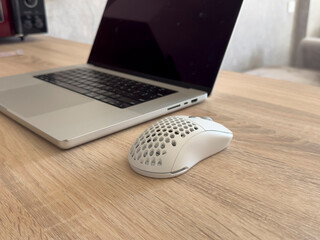 A computer mouse sits next to a laptop on a wooden surface in a light room