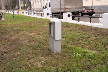 A utility box is positioned in the grass beside a road in an urban setting