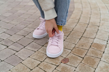 A person adjusts their shoelaces while standing on a stone surface in a park area