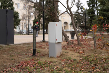 Utility box is situated on the ground in a park with trees and fallen leaves around it