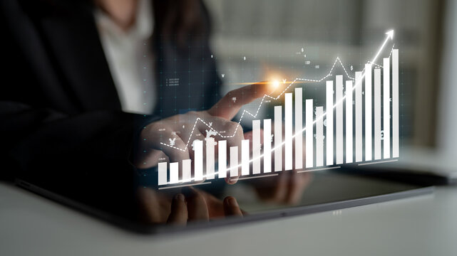 A professional in business attire interacts with a digital graph on a tablet, highlighting financial growth trends and data visualization in a modern office environment. Impute - Powered by Adobe