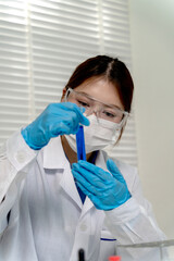 Asian adult scientist woman working lab examining blue test tube liquid for medical research and scientific discovery healthcare innovation development