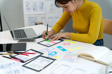 Asian young adult woman designer creating user interface experience prototypes with sketch mockups at home office for new mobile application development