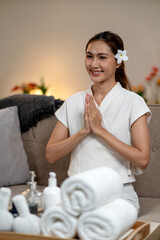 Smiling Asian woman spa therapist performs traditional wai gesture offering welcome and relaxation in a tranquil wellness center