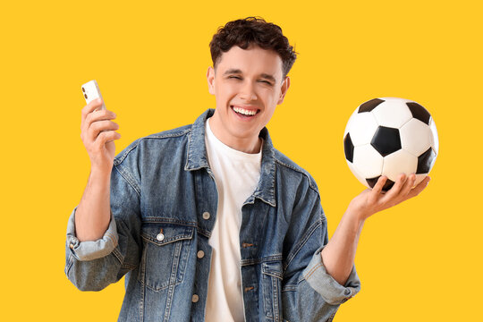 Happy young man with mobile phone and soccer ball on blue background. Sports bet concept
