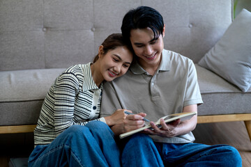 Asian adult couple enjoys writing notebook living room planning future creating shared memories cozy home environment happy intimate relationship bonding
