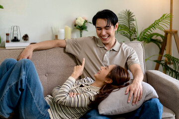 Asian adult couple laughing bonding relationship on sofa home cozy living room enjoy leisure time together inside modern house