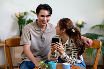 Asian adult couple sharing smartphone viewing content together talking smiling enjoying social interaction cafe leisure time connection discussing mobile communication