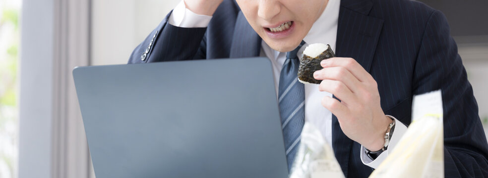 会社の休憩中に時間がなくてオニギリなどを急いでオフィスで食べる忙しい男性のビジネスシーン