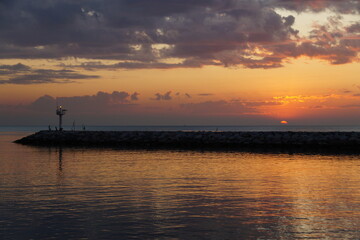 Naklejka premium The red ball of a huge sun rises from the horizon. The sky is painted a bright orange. Summer, morning twilight. Golden dawn on the sea.