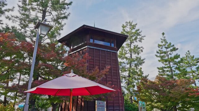 Wooden observation tower framed by autumn leaves, featuring a decorative light post and a red outdoor umbrella.