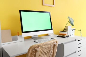 Modern computer with blank screen on table near yellow wall in home office, closeup