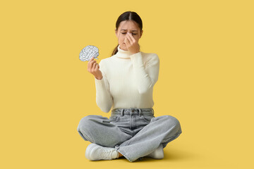 Young Asian woman with paper brain suffering from headache on yellow background. Brain Injury...