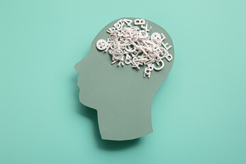 Paper human head with scrambled letters on turquoise background. World Mental Health Day