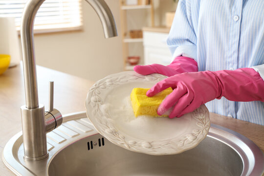Young woman washing dishes with housework sponge in kitchen sink