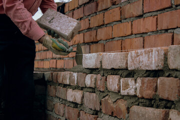Worker laying brick on mortar during wall construction