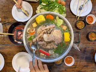 Sliced meat and vegetables cook in a metal grill pot filled with broth and steam, while the center...