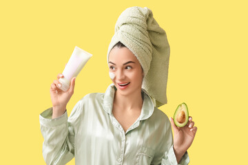 Beautiful young woman with tube of facial mask and fresh avocado on yellow background