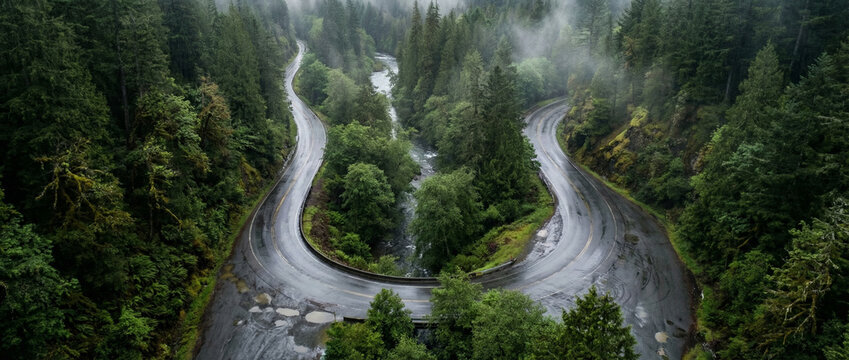 Aerial view winding road splits around river in lush green forest valley scenery