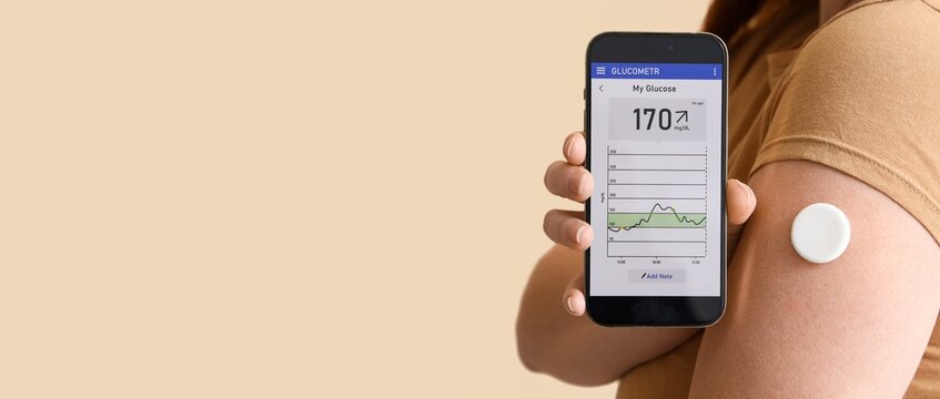Woman with glucose sensor using mobile phone for measuring blood sugar level on beige background with space for text, closeup