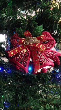 A glossy golden jingle bell decorated with a vibrant red bow and holly berries for holiday celebrations.