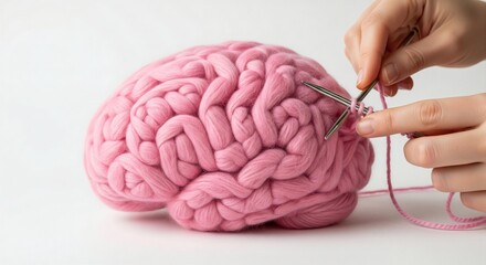 Human brain made of pink wool yarn being knitted with metal needles by hands on a white background. Conceptual studio photography. Creativity and mental health concept