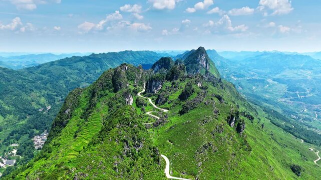 Aerial shot of a winding country road through a spectacular green mountain valley with rugged karst rock formations landscape in Guizhou