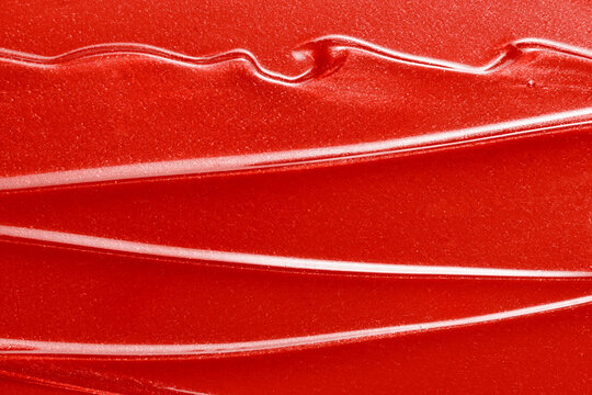 Lip gloss texture background.  Red shimmer liquid lipstick smeared closeup