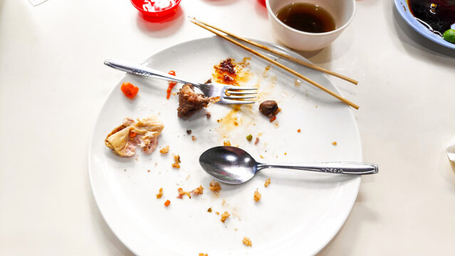 Close up photo of a dirty plate with leftover food scraps, used cutlery, and empty sauce bowls after a meal.